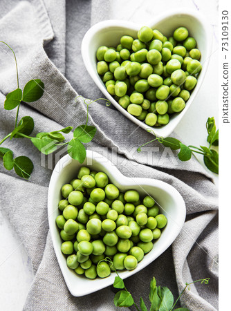 Green peas in heart shaped bowls on a fabric background 73109130