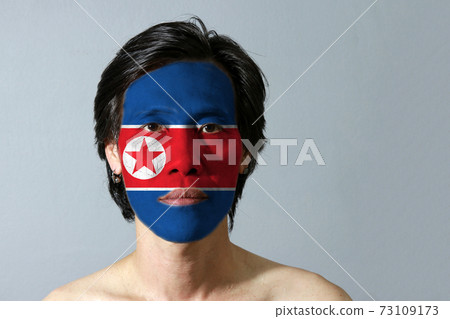 Portrait of a man with the flag of the North Korea painted on his face on black background. Portrait of a man with the flag of the North Korea painted on his face on black background. 73109173