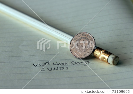 Two hundred Vietnam Dong coin on obverse (VND) with white pencil on the book. Two hundred Vietnam Dong coin on obverse (VND) with white pencil on the book. 73109665