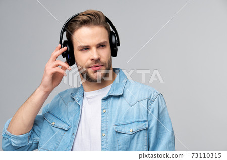 Close up portrait of cheerful young man enjoying listening to music wearing casual jeans outfit 73110315