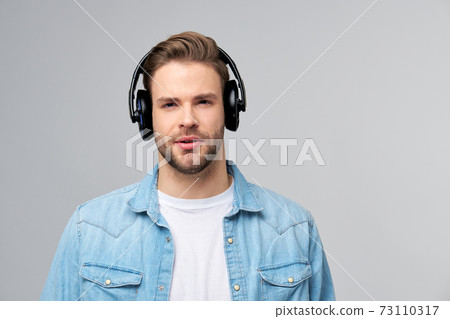 Close up portrait of cheerful young man enjoying listening to music wearing casual jeans outfit 73110317
