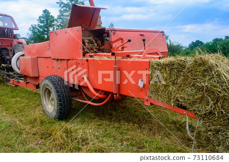 Old bale press, hay harvesting in the village for cattle, press work close up. Old bale press, hay harvesting in the village for cattle, press work close up. 73110684