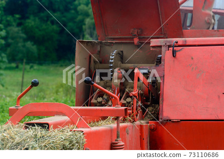 Old bale press, hay harvesting in the village for cattle, press work close up. 73110686