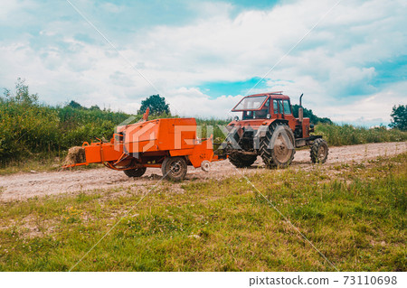 The process of harvesting hay for cattle, a tractor making bales in the field, old machinery. The process of harvesting hay for cattle, a tractor making bales in the field, old machinery. 73110698