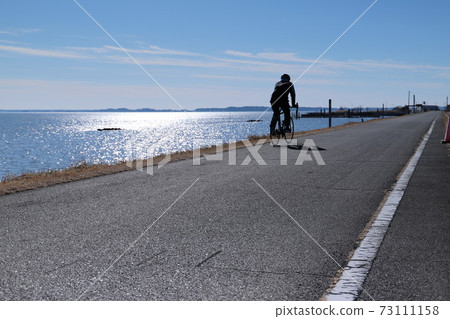 騎自行車的人在筑波霞浦Rinrin路上行駛,沐浴著霞浦反射的光 騎自行車的人在筑波霞浦Rinrin路上行駛,沐浴著霞浦反射的光 73111158