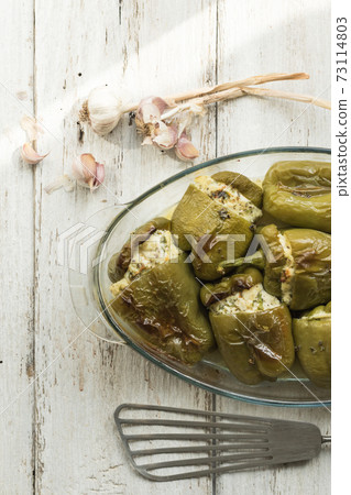 Pepper stuffed with white cheese, herbs, garlic. Glass dish prepared with seasonal local vegetables. White wood background. Soft focus 73114803
