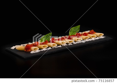 Select focus of an artistic arrangement of macaroni with cheese and tomato on a slate tray 73116857