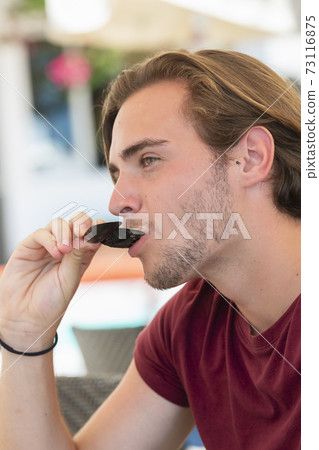 handsome young man eating a mussel from its shell on an out of focus background 73116875