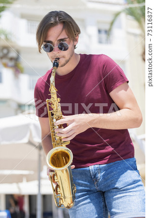 young man playing a saxophone while looking at the camera young man playing a saxophone while looking at the camera 73116877