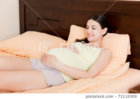pregnant woman sitting in bed and touching her belly at home. pregnancy expectation concept 73118309