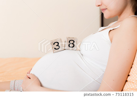 Pregnant woman in white underwear on bed in home holding calendar with weeks 38 of pregnant. Maternity concept. Expecting an upcoming baby Pregnant woman in white underwear on bed in home holding calendar with weeks 38 of pregnant. Maternity concept. Expecting an upcoming baby 73118315