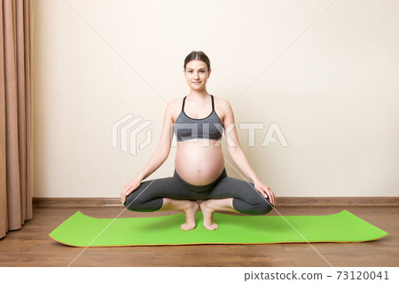 beautiful young pregnant woman sitting on mat in yoga pose at the home. Pregnancy Yoga and Fitness concept at coronavirus time 73120041