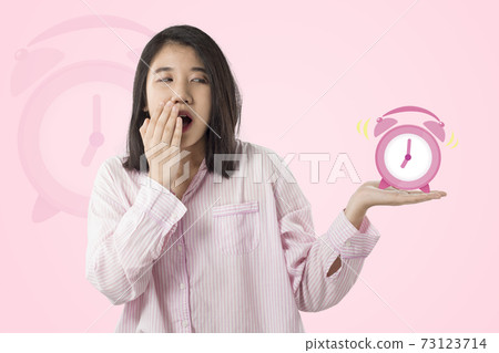 woman wear pink pajamas yawn and holding alarm clock  feeling sleepy 73123714