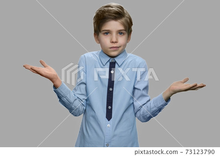 Boy shrugging shoulders against gray background. Boy shrugging shoulders against gray background. 73123790