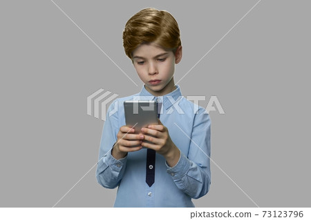 Little caucasian boy using smartphone on gray background. Little caucasian boy using smartphone on gray background. 73123796
