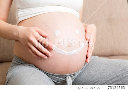 a pregnant girl sits at home on the bed and smears smile an anti-stretch mark cream on her stomach. Pregnancy, motherhood, preparation and expectation concept a pregnant girl sits at home on the bed and smears smile an anti-stretch mark cream on her stomach. Pregnancy, motherhood, preparation and expectation concept 73124563