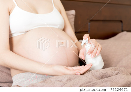 a pregnant girl sits at home on the bed and smears smile an anti-stretch mark cream on her stomach. Pregnancy, motherhood, preparation and expectation concept a pregnant girl sits at home on the bed and smears smile an anti-stretch mark cream on her stomach. Pregnancy, motherhood, preparation and expectation concept 73124671