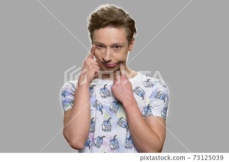 Funny teenage boy grimacing on gray background. 73125039