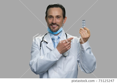 Male caucasian doctor showing pills on gray background. Male caucasian doctor showing pills on gray background. 73125247