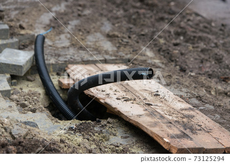 Thin diameter ribbed black PVC pipe in the ground before laying Thin diameter ribbed black PVC pipe in the ground before laying 73125294