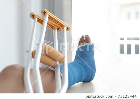 Blue ankle and foot splint Bandages on the legs from a young man's fall accident, Blue plaster on the ankle, Crutches assist in the walking of the patient. 73125444