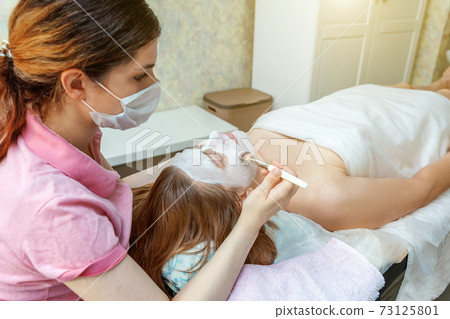 Woman getting face treatment with white nourishing creme in spa salon 73125801