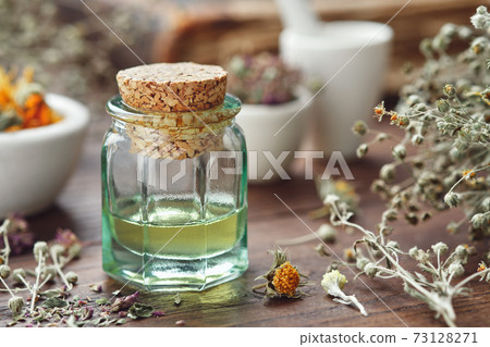 Essential oil bottle, mortars of dry medicinal herbs and old book on background. Essential oil bottle, mortars of dry medicinal herbs and old book on background. 73128271