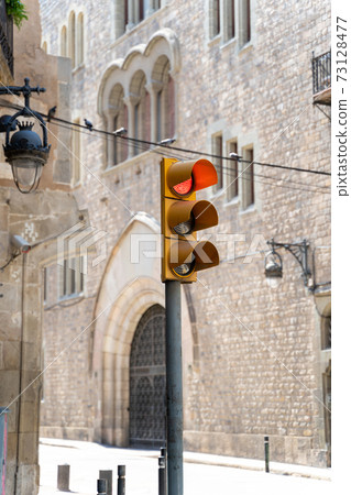 Yellow traffic light showing red on street with medieval buildings in Barcelona 73128477