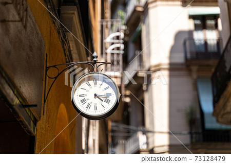 Street clock with arrows on wall with background of buildings in Barcelona Street clock with arrows on wall with background of buildings in Barcelona 73128479