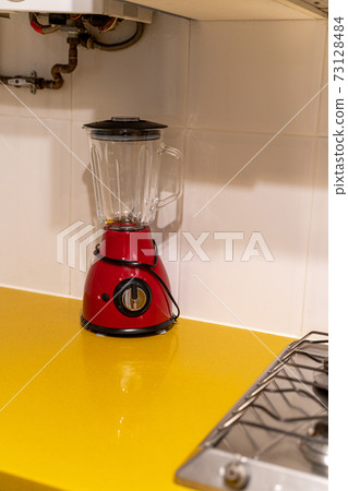 Red electronic mixer stands on a yellow table near the stove in the kitchen Red electronic mixer stands on a yellow table near the stove in the kitchen 73128484