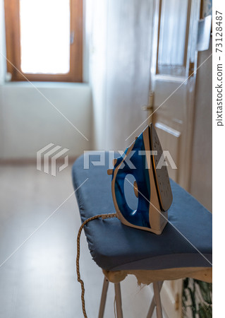 Modern electric iron on board by the door and bright window with daylight Modern electric iron on board by the door and bright window with daylight 73128487