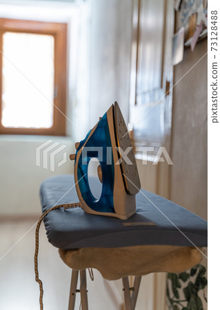 Modern electric iron on board by the door and bright window with daylight Modern electric iron on board by the door and bright window with daylight 73128488