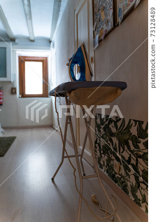 Modern electric iron on board by the door and bright window with daylight Modern electric iron on board by the door and bright window with daylight 73128489