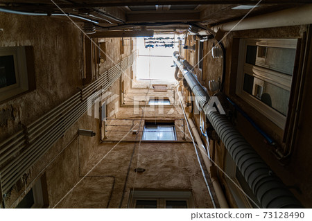 Well in courtyard of old buildings with windows, pipes and daylight 73128490