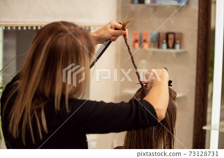 View fron the back of hairdresser trimming blond long hair with scissors in hair salon View fron the back of hairdresser trimming blond long hair with scissors in hair salon 73128731