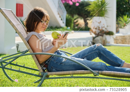 Beautiful mature woman resting on sunbed on green lawn. 73128905