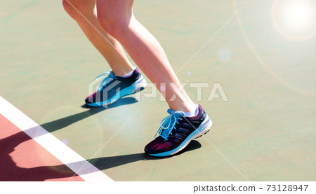 Legs of young girl in a closed tennis court with racket, sport shoes Legs of young girl in a closed tennis court with racket, sport shoes 73128947