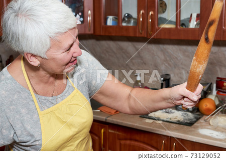 Woman with gray hair holding a wooden rolling pin in her hand Woman with gray hair holding a wooden rolling pin in her hand 73129052