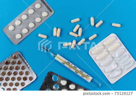 glass thermometer, white capsules and pills in packaging on a blue background 73129127