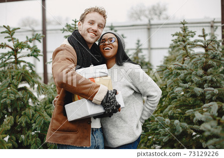 Mixed couple standing with gifts by the Christmas tree 73129226