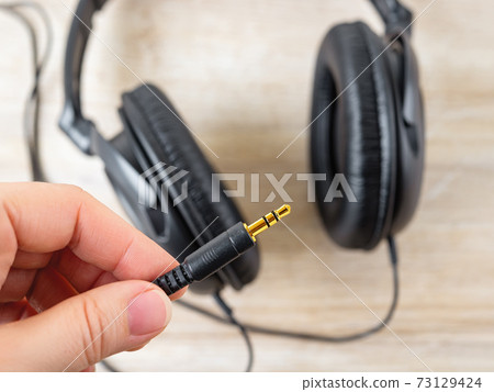 Fingers holg golden TRS jack of black wired over ear headphones. 73129424