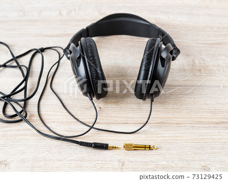 Black wired over ear headphones nead golden TRS adapter and jack on a desk.  73129425