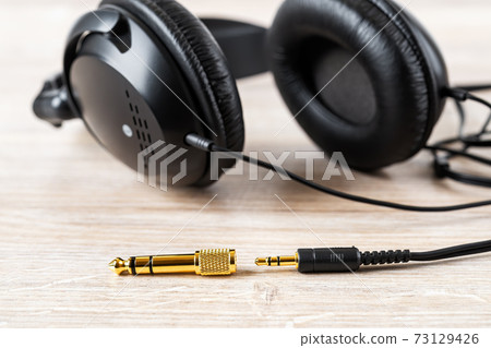 Golden TRS adapter and jack near black wired over ear headphones on a desk. 73129426