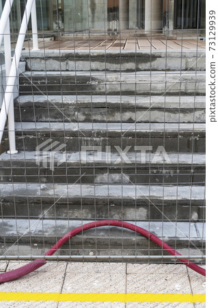 A mesh fence in front of a concrete staircase at a construction site. No entry. Abandoned red electrical plastic cable duct. Occupational safety and health concept A mesh fence in front of a concrete staircase at a construction site. No entry. Abandoned red electrical plastic cable duct. Occupational safety and health concept 73129939