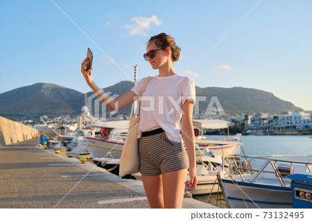 Fashionable beautiful girl teenager walking on pier, sunset on sea Fashionable beautiful girl teenager walking on pier, sunset on sea 73132495