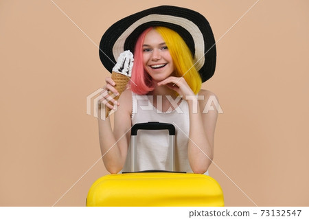 Young happy teen girl in hat with suitcase eating ice cream 73132547