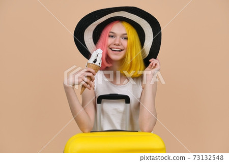 Young happy teen girl in hat with suitcase eating ice cream 73132548