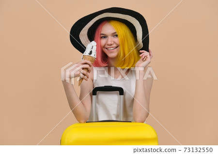Young happy teen girl in hat with suitcase eating ice cream 73132550