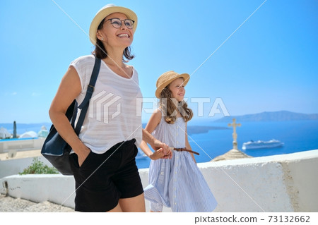 Happy tourists family mother and daughter kid walking on the Greek island of Santorini Happy tourists family mother and daughter kid walking on the Greek island of Santorini 73132662