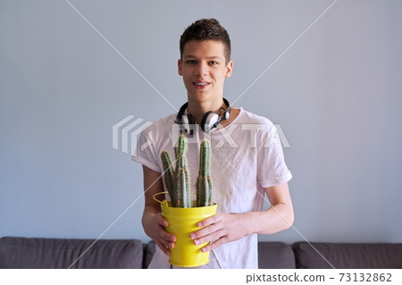 Portrait of teenage boy in headphones holding pot of cacti in his hands 73132862